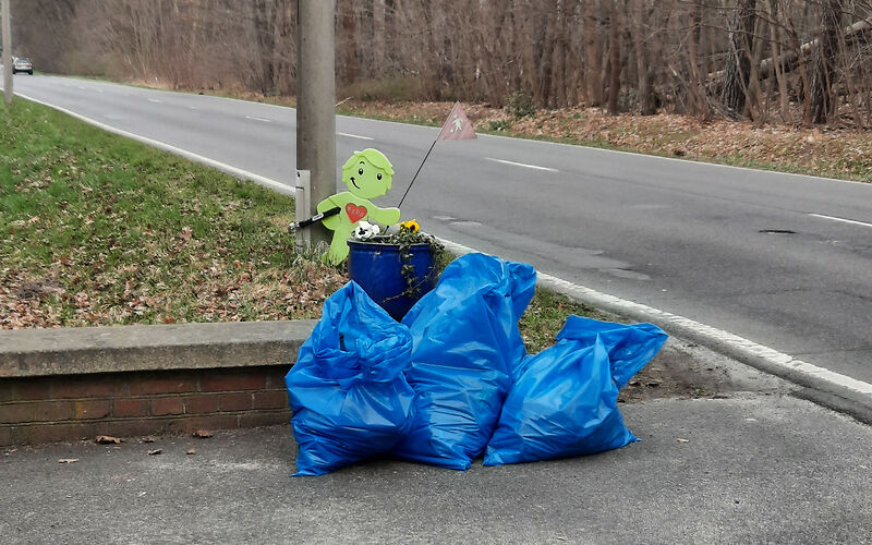 3 blauen Müllsäcke neben vor einem grünen Aufsteller, der ein Kind darstellt.