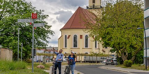 Zwei Radfahrende stehen am Knotenpunkt 25. Im Hintergrund ist die Stadtkirche St. Nikolai zu sehen.