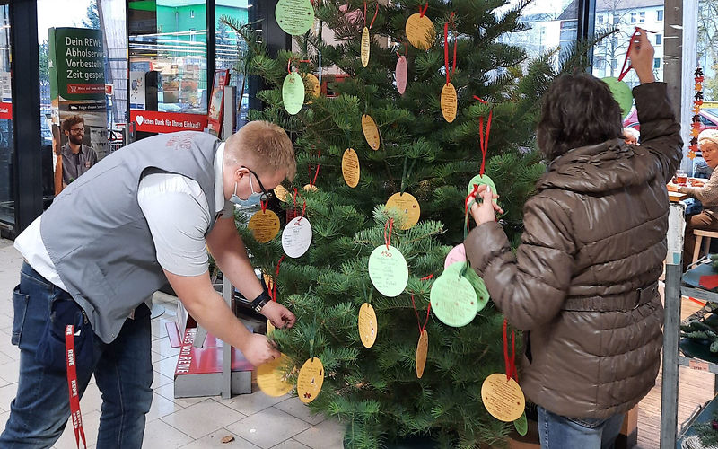 Wunschbaum im REWE Markt wird mit Papierkugeln geschmückt, auf denen Wünsche geschrieben stehen