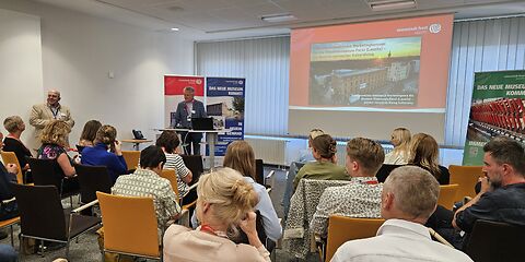 Der Präsident der Euroregion Spree-Neisse Czesław Fiedorowicz steht vor dem Pult neben der Präsentation und begrüßt die Gästeür 