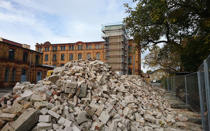 Sicht auf den Hof des Museums auf die Außenansicht des eingerüsteter Fahrstuhlschacht am Hauptgebäude, zu sehen ist auch ein großer Bauschutt im Vordergrund