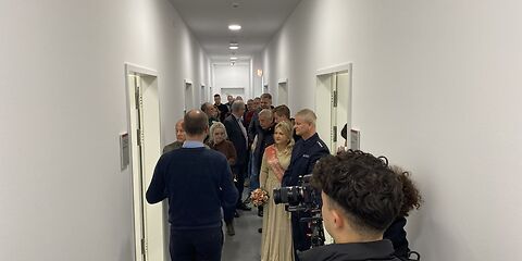 Rundgang durch das Archiv: Die Gruppe steht in einem schmalen weißen Flur, in dem links und rechts mehre Türen befinden.