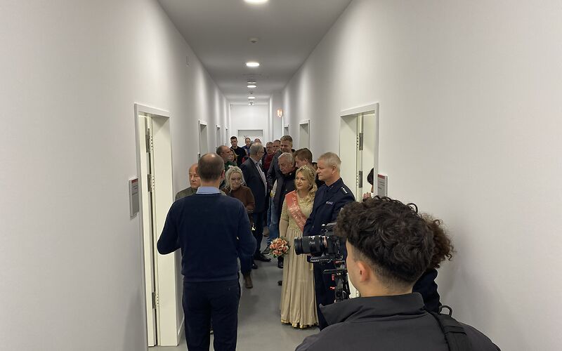 Rundgang durch das Archiv: Die Gruppe steht in einem schmalen weißen Flur, in dem links und rechts mehre Türen befinden.