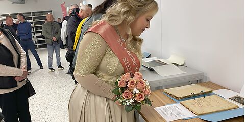 Die Rosenkönigin betrachte ausgestellte Archivarien, die auf einem Tisch liegen.