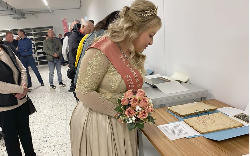 Die Rosenkönigin betrachte ausgestellte Archivarien, die auf einem Tisch liegen.