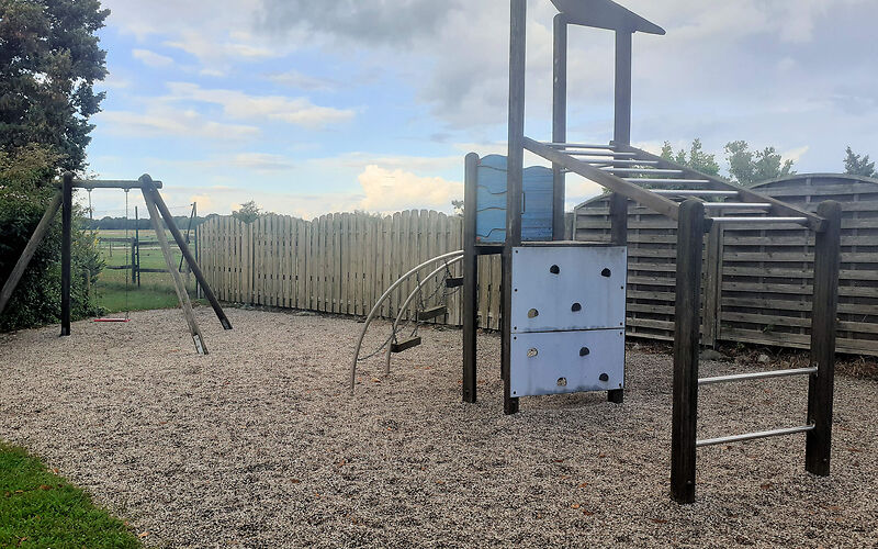 Rechts steht ein Klettergerüst mit mehreren wagerecht an Holzstangen befestigten Metallstäben und einem dreieckigen Turm aus Holz.