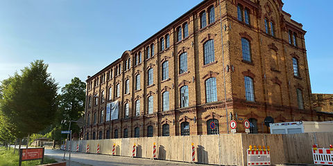 Blick auf das Hauptgebäude, fester Bauzaun rings um das Gebäude entlang der Sorauer Straße