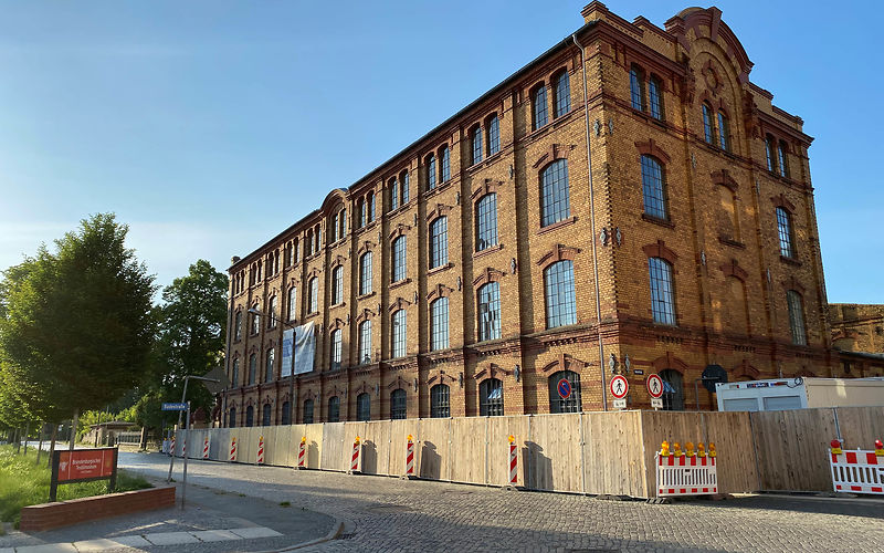 Blick auf das Hauptgebäude, fester Bauzaun rings um das Gebäude entlang der Sorauer Straße
