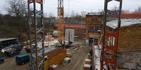 Blick in den Innenhof, zu sehen sind Baumaterialien, ein Fahrzeug, ein Baucontainer, drei Baukräne, rechtsseitig stehen Gebäude mit einer Rüstung.