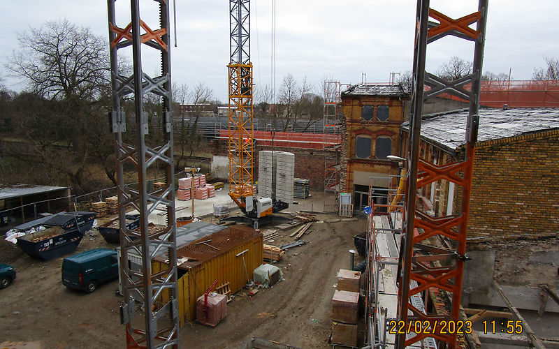 Blick in den Innenhof, zu sehen sind Baumaterialien, ein Fahrzeug, ein Baucontainer, drei Baukräne, rechtsseitig stehen Gebäude mit einer Rüstung.