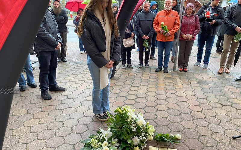 Eine Schülerin steht vor den Stolpersteinen während der Gedenkveranstaltung. Um die Steine herum liegen Blumen.