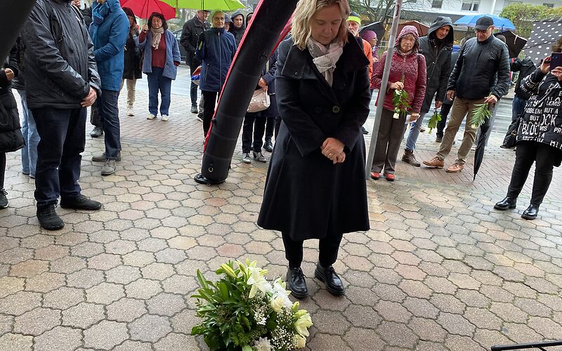 Die Bürgermeisterin steht vor den Stolpersteinen mit gesenktem Blick und verschränkten Händen.