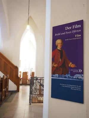 Hinweistafel auf die Dauerausstellung in der Stadtkirche St. Nikolai, Fotograf: LinaMedia, Copyright: LinaMedia Teil-Innanansicht Stadtkirche St. Nikolai, Hinweistafel auf die Dauerausstellung lila Hintergrund mit Abbildung des Grafen Brühl
