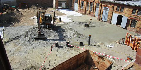 Herstellen der Hofbefestigung: Blick aus dem 3. OG des Hauptgebäudes in den Hof, im Vordergrund steht ein Container für den Abbruch Fußboden aus dem 3. OG Hauptgebäude, in der Mitte des Hofes arbeitet der Bagger und verteilt den Schotter