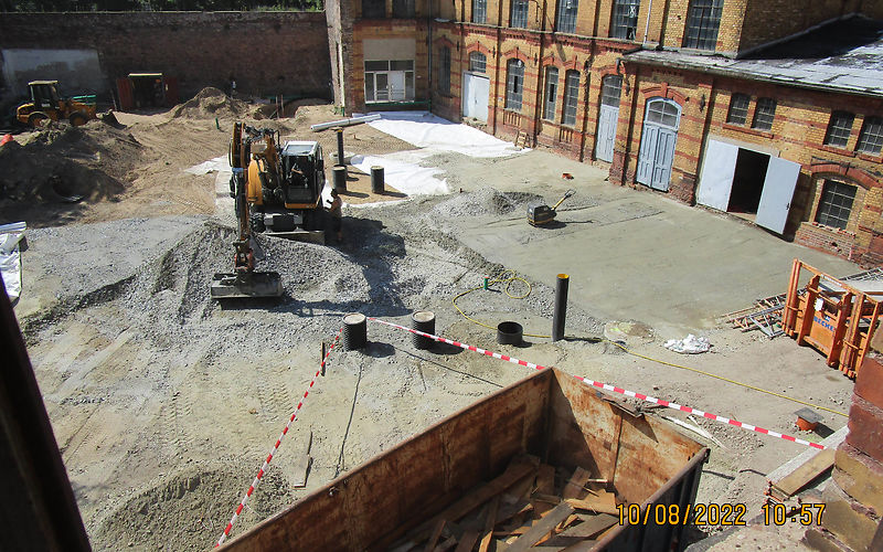 Herstellen der Hofbefestigung: Blick aus dem 3. OG des Hauptgebäudes in den Hof, im Vordergrund steht ein Container für den Abbruch Fußboden aus dem 3. OG Hauptgebäude, in der Mitte des Hofes arbeitet der Bagger und verteilt den Schotter