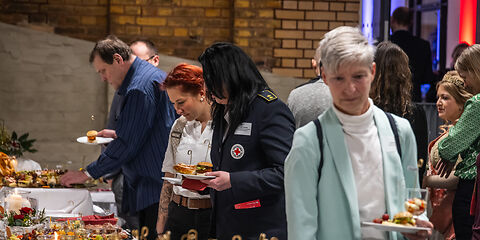 Die Gäste nehmen sich etwas vom Buffet, u.a. gibt es Burger, belegte Brötchen und Gebäck. 