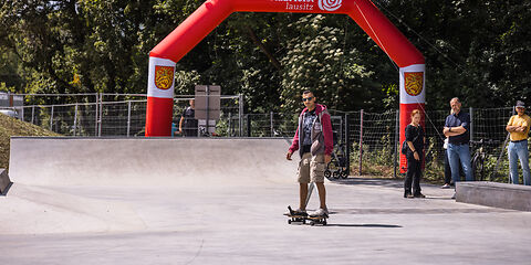 Mann mit Sonnenbrille fährt auf Skateboard in Skatepark vor rotem aufblasbarem Tor mit Schriftzug 'rosenstadt forst lausitz'
