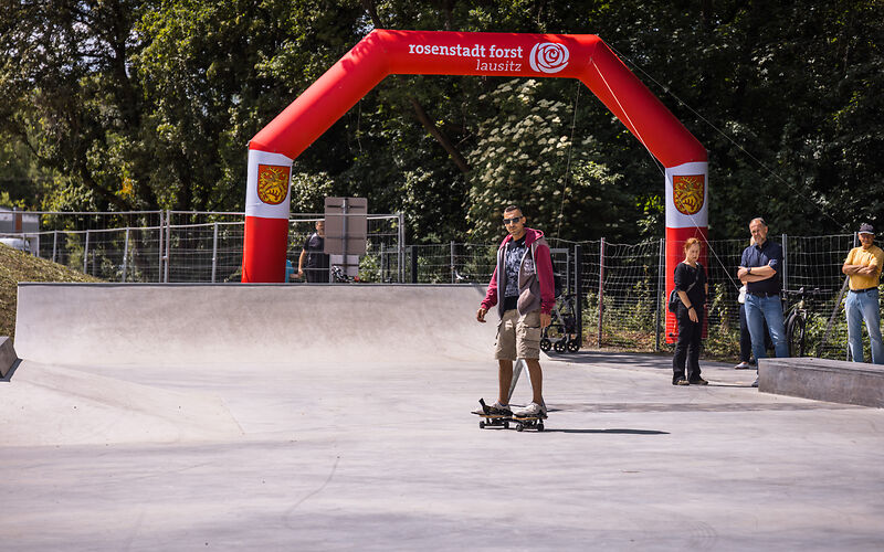 Mann mit Sonnenbrille fährt auf Skateboard in Skatepark vor rotem aufblasbarem Tor mit Schriftzug 'rosenstadt forst lausitz'