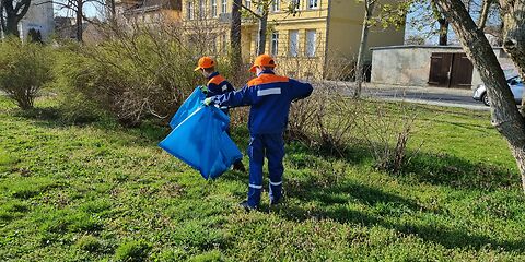 Zwei Kinder aus der Jugendfeuerwehr sammeln in blauer Unifvorm Müll auf einer Wiese. 