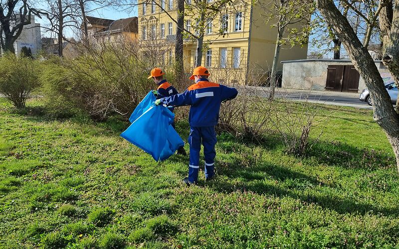 Zwei Kinder aus der Jugendfeuerwehr sammeln in blauer Unifvorm Müll auf einer Wiese. 
