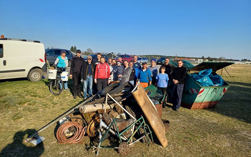 Die Mitglieder des LTSV Forst 1990 e.V. stehen hinter einem Schrottberg aus u. a. Reifen, Schläuchen, einem Fahrradrahmen. Rechts im Bild steht ein großer Müllcontainer, der mit blauen Säcken vgefüllt ist.