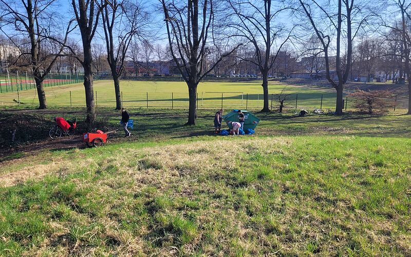 Auf der Wiese vor einem Sportplatz sind mehrere Personen mit Bollerwagen, die Müll sammeln.