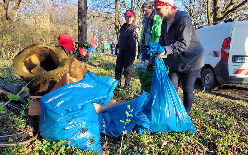 Mehrere Personen tragen Schrott und sonstigen Müll zu einem Sammelpunkt. Der Müll ist teilweise in Säcken verpackt. 
