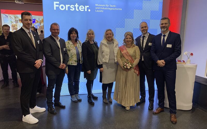 Die Bürgermeisterin und die Rosenkönigin stehen mit mehreren der Teilnehmenden vor ein blauen Leinwand mit der Aufschrift 