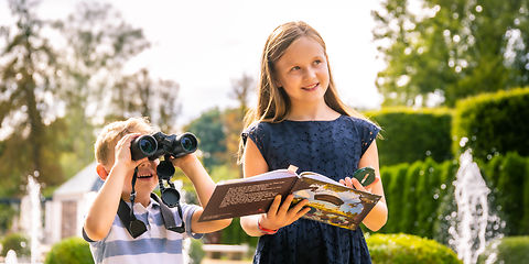 Junge und Mädchen entdecken den Rosenpark, Mädchen hälte ein Buch und einen Kompass in der Hand, Junge schaut in ein Fernglas, im Hintergrund Fontänen der Großen Wasserspiele