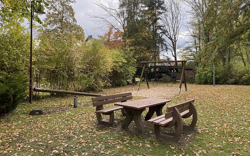 Im Vordergrund befindet sich ein Holztisch mit zwei Bänken, dahinter steht eine Holzwippe.