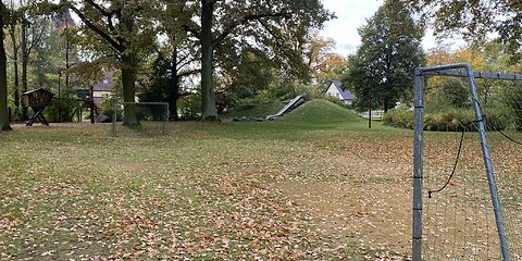 Zwei Fußballtore stehen auf einer Wiese gegenüber, im Hintergrund befindet sich auf an einem Hügel eine Rutsche.