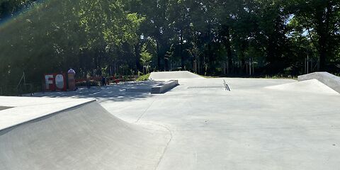 Leere Skateanlage mit Betonrampen vor einem Hintergrund aus Bäumen bei Sonnenschein