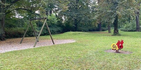 Eine Schaukel mit einem Holzgestell auf einer Sandfläche und eine Federwippe in Form eine Schnecke.