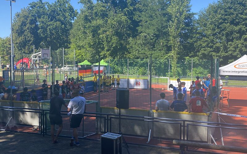 Auf dem eingezäunten Fußballfeld mit kleinen Toren, haben sich die Mannschaften an den Seitenrändern aufgestellt.