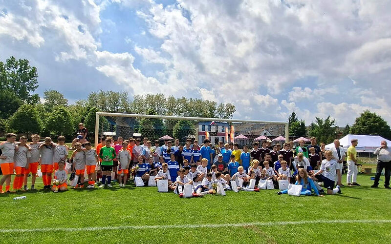 Gruppenbild vor dem Fußballtor, die Spieler, die vorn sitzen haben weiße Tüten vor sich stehen, zwei von ihnen haben einen Pokal..